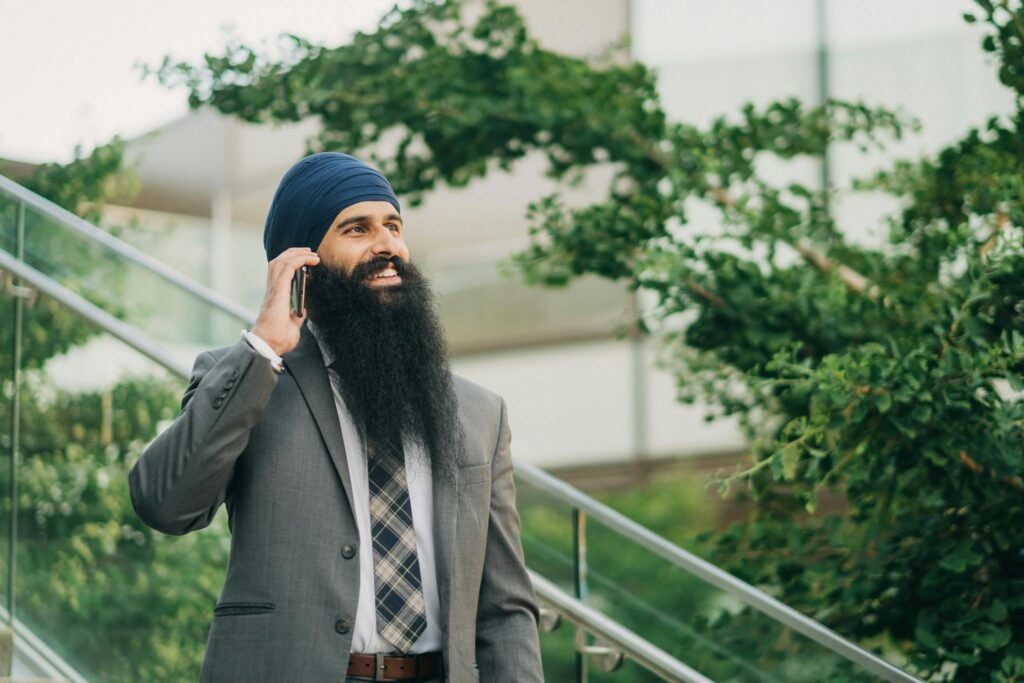 Businessman in a suit talking on a smartphone outdoors with greenery background.